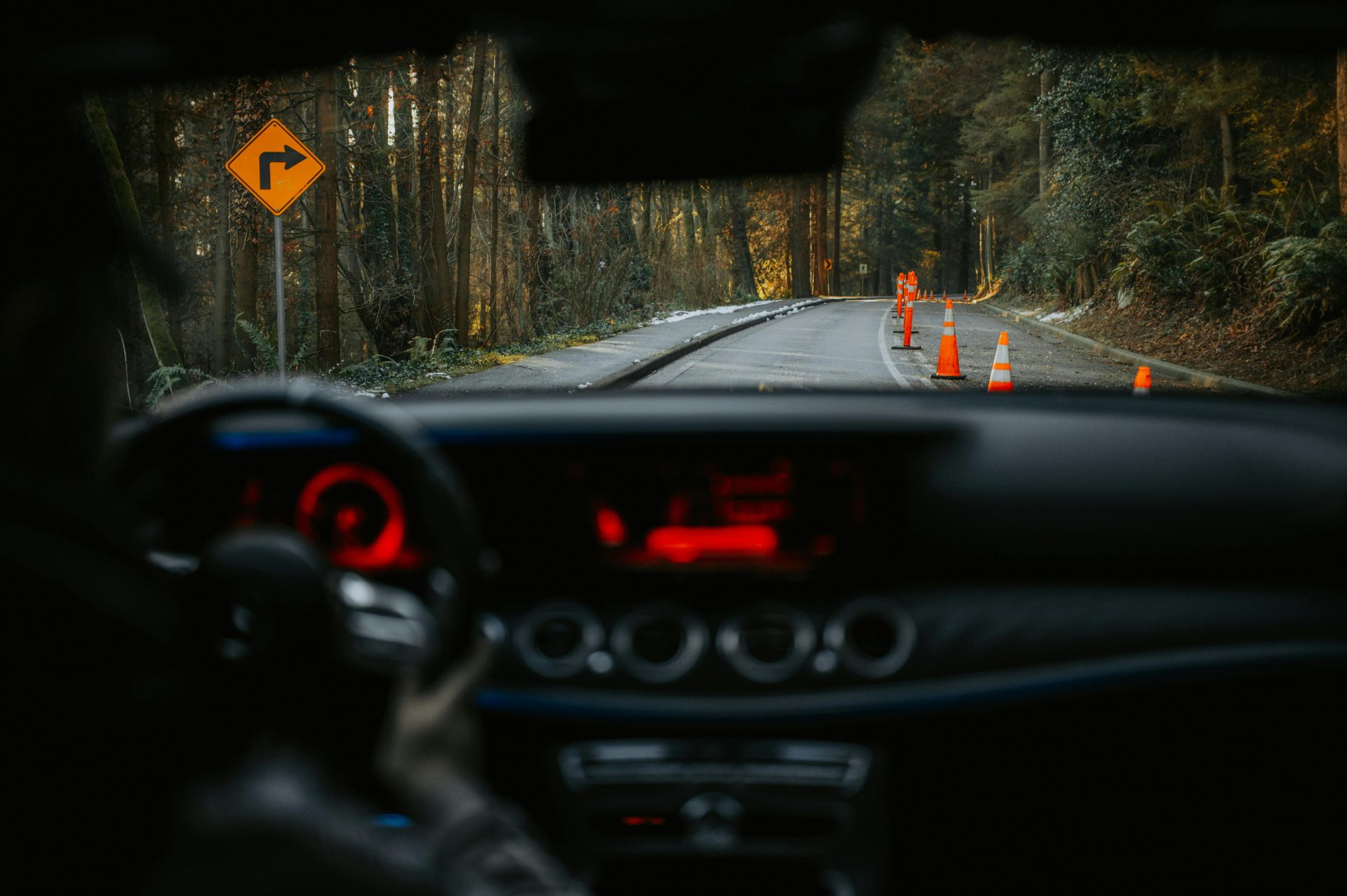 View from car dashboard of rural road with traffic cones and turn sign. Scenic forest driving experience.