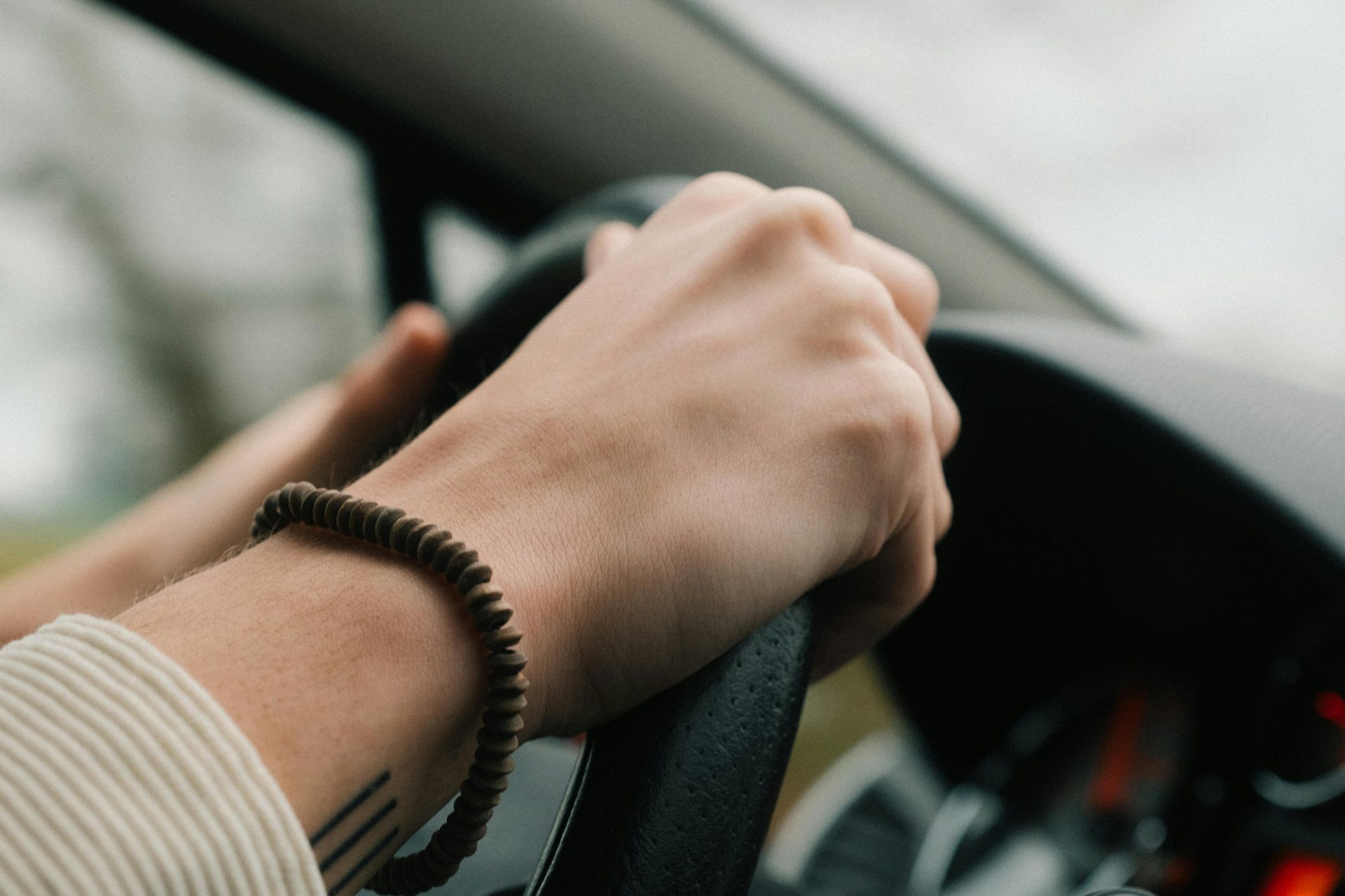 Detail of hands holding car steering wheel, wearing bracelet, while driving