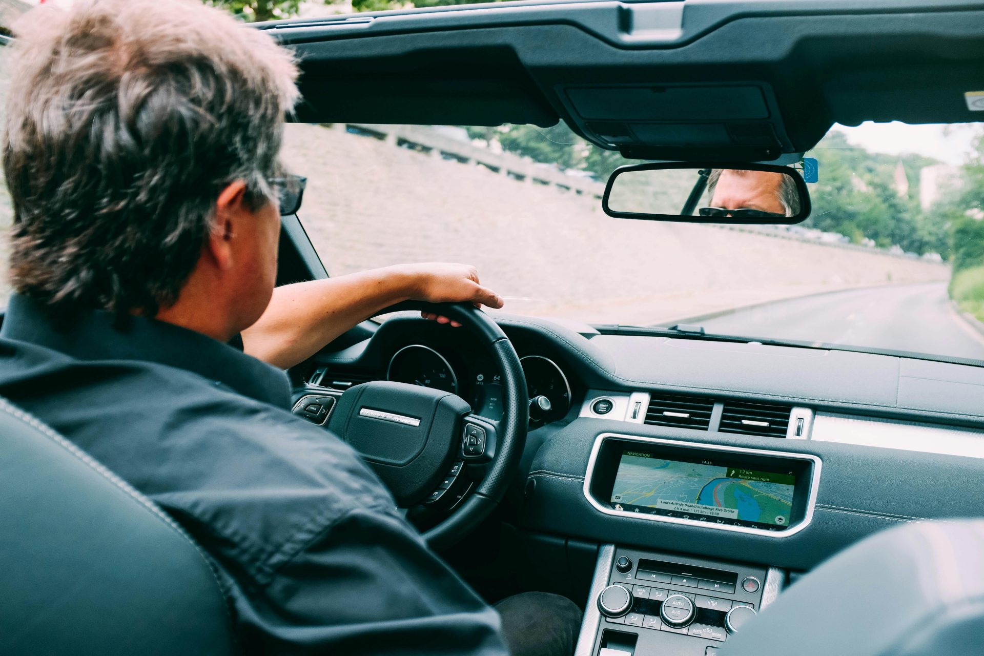 A man driving a convertible car on a scenic highway with a focus on the dashboard.