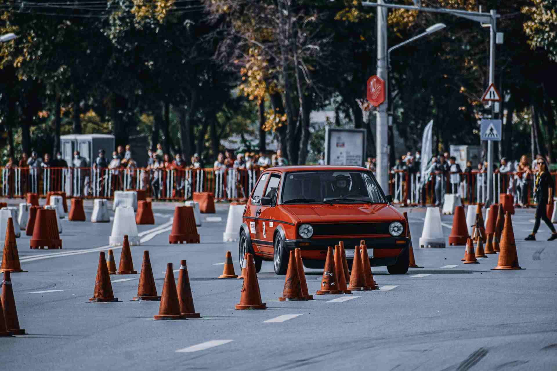 Unrecognizable person driving red spots car on asphalt road with orange road cones during competition in daytime