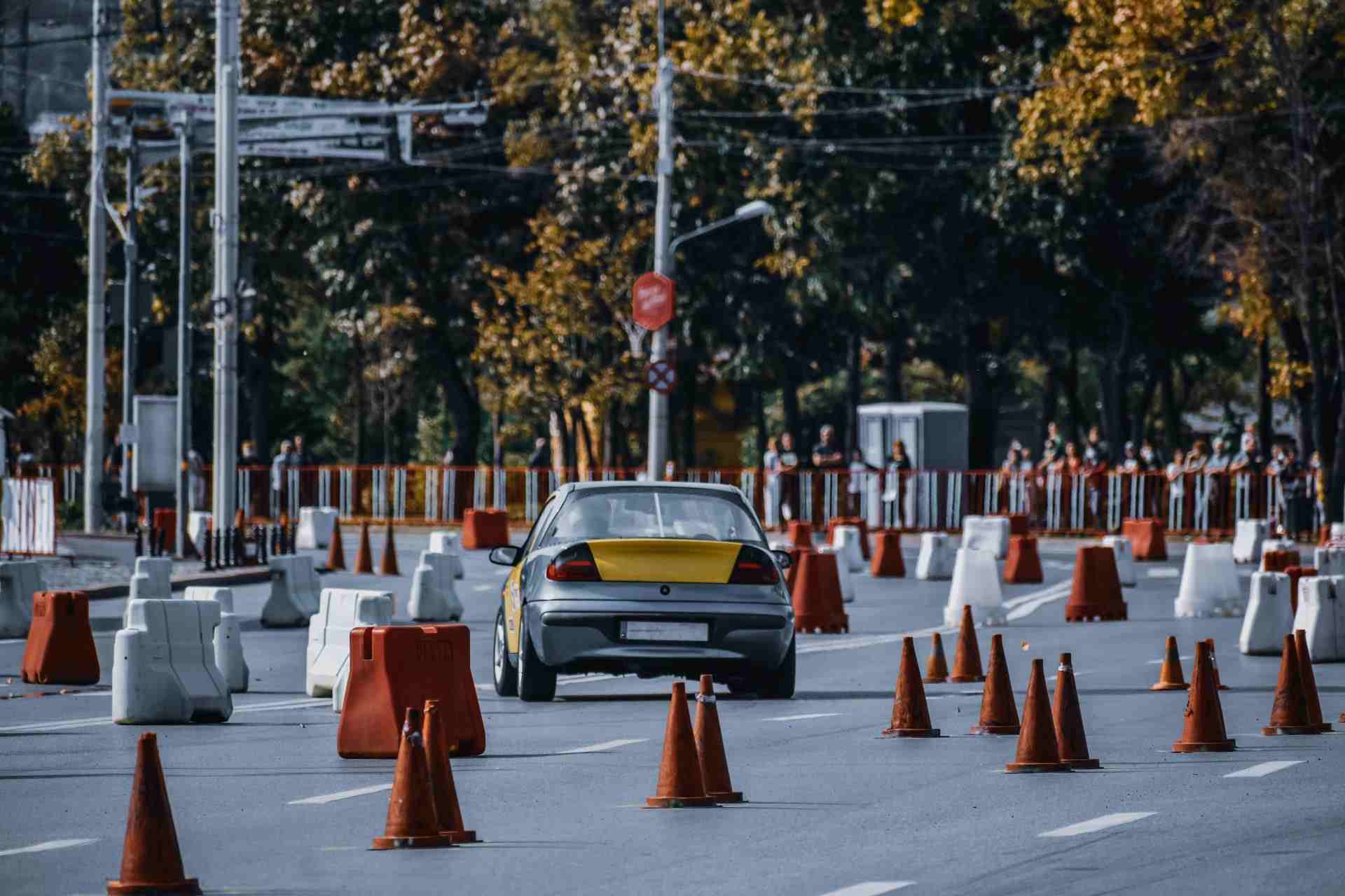 Participant in car race maneuvering between red and white traffic cones or barriers in front of audience